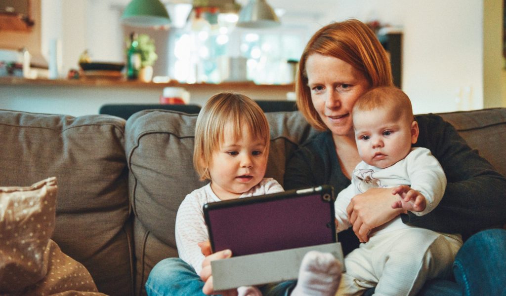 young woman with children on her lap looking at ipad